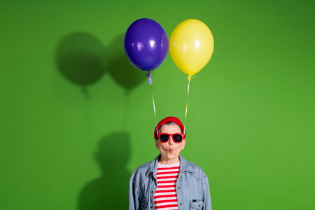 Playful Person Posing Against a Green Background with Balloons in a Stylish Casual Attire