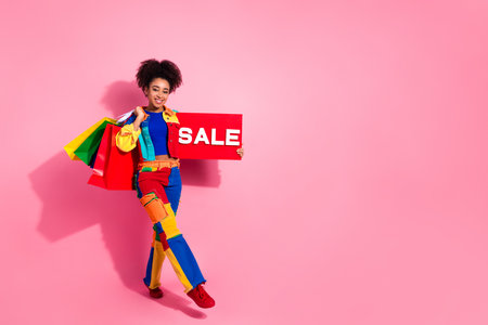 Colorful stylish woman holding sale sign and shopping bags against a pink backgroundの写真素材