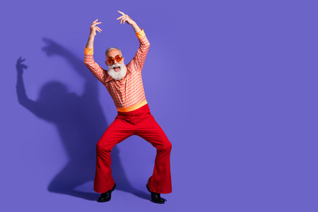 Mature man with grey beard in retro fashion poses energetically against violet backdrop showing dance gestures and charismaの写真素材
