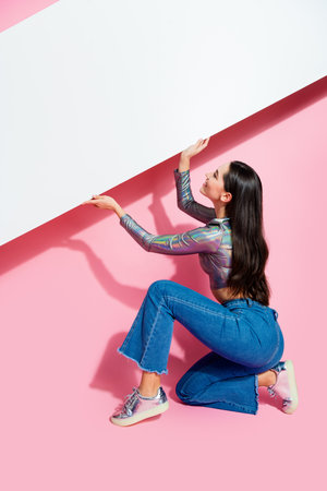 Stylish young woman in trendy attire posing against a vibrant pink background with a blank propの写真素材