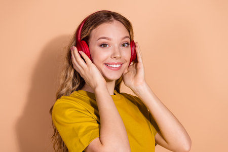 Smiling young woman listening to music with red headphones against a beige background