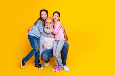 Happy grandfather and his two young granddaughters posing together in casual outfits on a yellow backgroundの写真素材