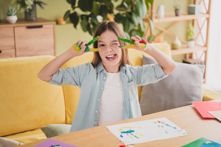 Smiling young girl having fun with finger paint in a cozy living room settingの写真素材