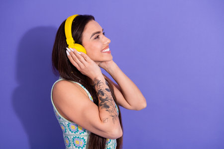 Attractive young woman with long brunette hair enjoying music with yellow headphones against a vibrant purple backgroundの写真素材