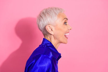 Smiling senior woman with short white hair in blue shirt against vibrant pink background, expressing happiness and positivityの写真素材