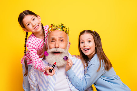 Happy grandfather and granddaughters having fun and sharing joyful moments together against a vibrant yellow backgroundの写真素材
