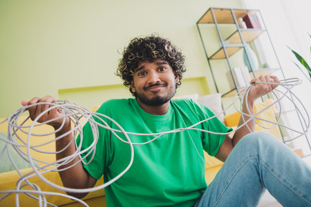 Photo of nice young man shrug shoulders hold messy tied cable wear t-shirt modern green interior...