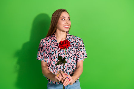 Portrait of an Attractive Young Woman Holding a Red Rose Against a Vibrant Green Background, Wearing a Stylish Leopard Print Shirtの写真素材