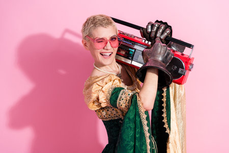 Young woman in medieval-inspired costume with modern accessories holding boombox against pink...