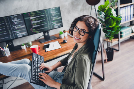 Young woman working remotely as a programmer in a casual setting, smiling confidently at her modern...