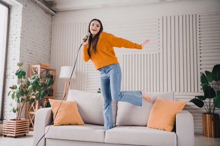 Cheerful woman Singing Joyfully at Home with a Microphone on a Comfortable Couch in a Bright and Stylish Living Room Filled with Daylightの写真素材