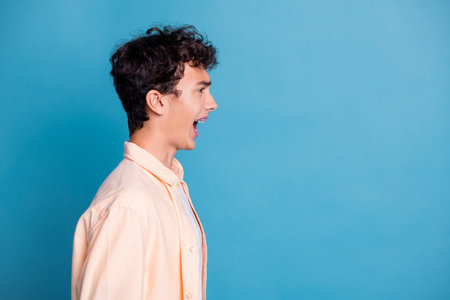 Young man with curly hair wearing a stylish casual shirt against a blue background, expressing joy and happiness.の写真素材
