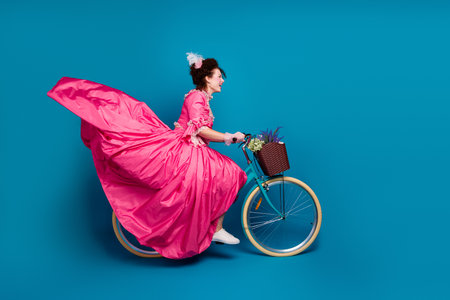 Full length photo of happy attractive lady dressed baroque costume driving cycle copy space isolated blue color backgroundの写真素材