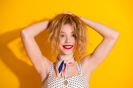 Cheerful young woman posing against a vibrant yellow background, showcasing a playful smile and trendy summer fashionの写真素材