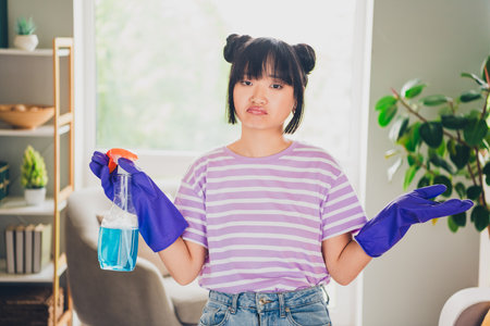 Photo of cute doubtful girl dressed purple striped t-shirt dislike cleaning indoors house apartment roomの写真素材