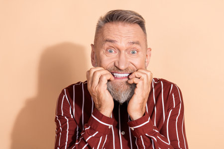 Portrait of an expressive elderly man with a beaming smile highlighting his emotions against a beige backgroundの写真素材