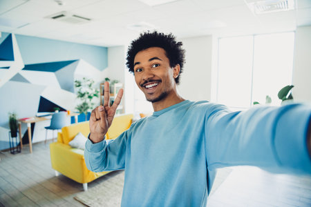 Smiling young man taking a selfie in a stylish modern living room with a vibrant interior design and...