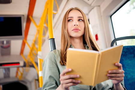 Young woman reading a book during her bus ride through a vibrant urban city