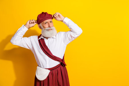 Portrait of a cheerful senior man wearing traditional Scottish attire in a joyful pose against a vibrant yellow backgroundの写真素材