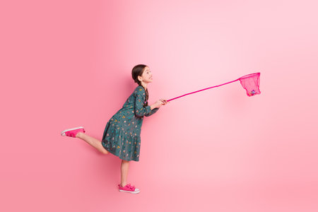 Happy young girl with braided hair playing with playful enthusiasm against a vibrant pink background in stylish attireの写真素材