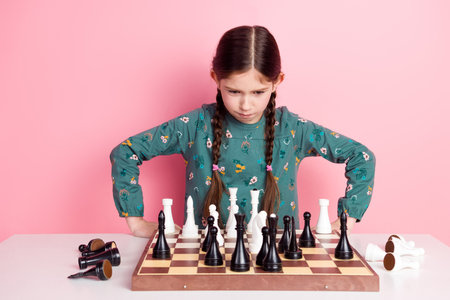 Thoughtful young girl concentrating on chess strategy at a table with playful pink backgroundの写真素材