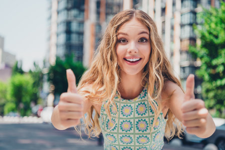 Happy young woman giving thumbs up in sunny urban setting showcasing vibrant fashion and charm