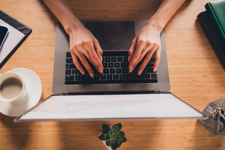 Young professional woman working on laptop in modern office setting with natural daylightの写真素材