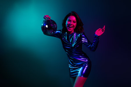 Portrait of stunning young girl hold disco ball wear shiny dress neon light dark blue background