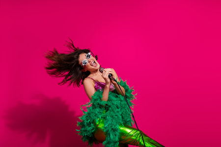 Fashionable young woman celebrating and singing passionately on a mic, vibrant pink backdrop, modern...