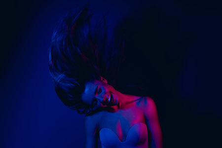 Young woman in neon blue and pink lighting with dynamic hair and confident pose representing beauty, fashion, and nightlifeの写真素材