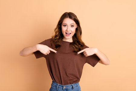 Playful young woman showing a fun gesture on a beige background, capturing a joyful and stylish moment in casual fashionの写真素材