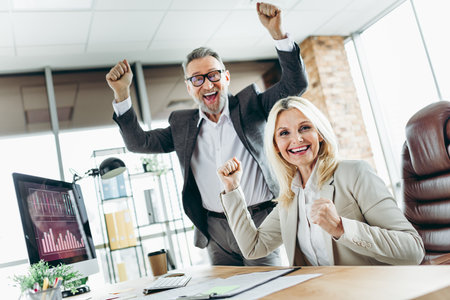 Professional businessman and businesswoman celebrating success with excitement in an office workspace settingの写真素材