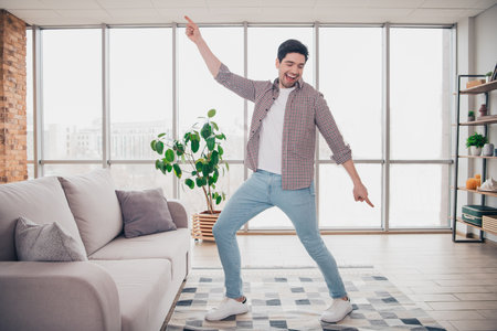 Young man dancing joyfully in a modern living room with cozy furnishings and vibrant energy during a leisure day indoorsの写真素材