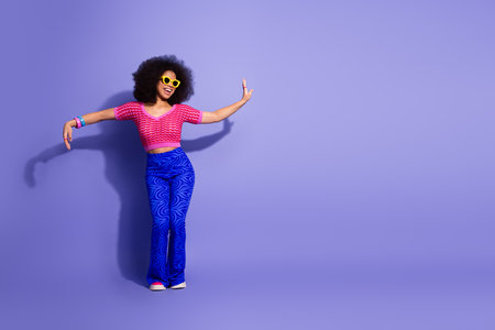 Stylish young woman showcases colorful retro fashion with vibrant outfit and joyful expression against a purple backdropの写真素材