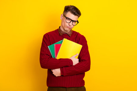 Intelligent student Man Holding Notebooks Against Yellow Background in Casual Red Sweaterの写真素材
