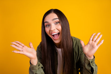Happy young woman in casual attire gesturing with a cheerful expression against a vibrant yellow...