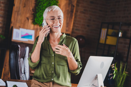 Photo of charming cheerful lady dressed shirt eyewear speak phone workplace loft interior indoorsの写真素材