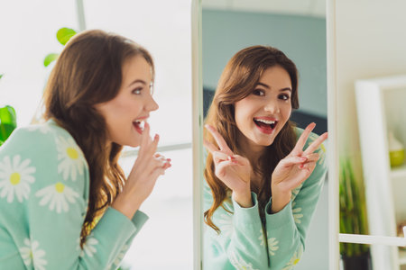 Young woman poses happily in front of a mirror at home wearing a patterned cardigan in a bright indoor settingの写真素材