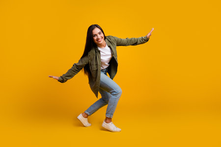 Happy young woman in casual outfit posing playfully against yellow background, expressing joy and positivity with her charming smileの写真素材