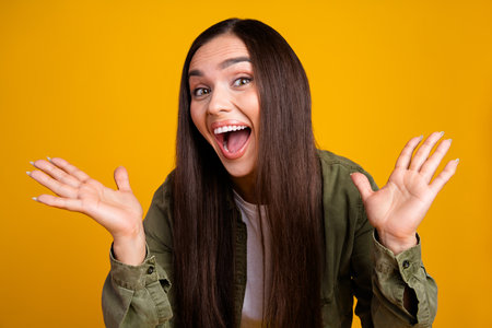 Cheerful brunette woman in casual outfit posing and expressing excitement against bright yellow studio backgroundの写真素材