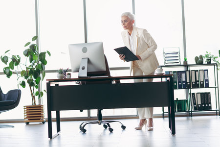 Elegant professional businesswoman in modern office workspace with natural light and plants contributing to productive atmosphereの写真素材