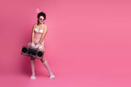 Young woman in elegant corset dress with boombox against pink background. Blends retro fashion with...