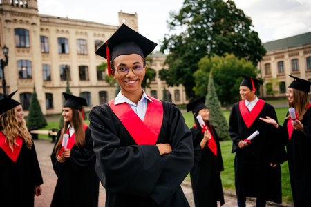 Joyful group of young graduates celebrating in caps and gowns outdoors on a summer day after receiving their degrees at university campusの写真素材