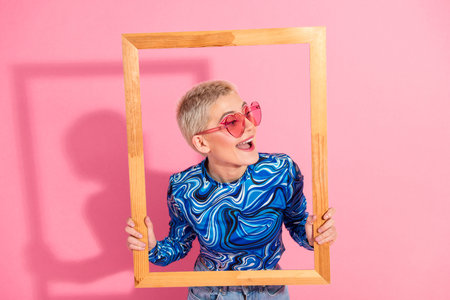 Fashionable young woman with blonde short hair wearing stylish clothes posed playfully with a wooden...