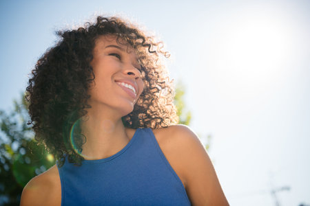Joyful young woman enjoying a sunny day outdoors, capturing the essence of happiness and freedom, smiling brightly in a casual blue outfitの写真素材