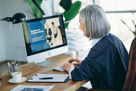 Mature businesswoman in professional workspace looking at computer-based presentation for business...