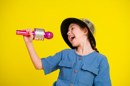 Charming young girl enjoying and singing with a pink microphone on a vibrant yellow backdrop, exuding happiness and creativity.の写真素材