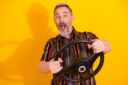 Charismatic middle aged man holding a large steering wheel on a vibrant yellow background