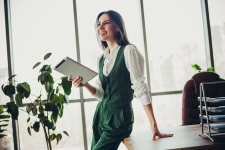 Confident professional businesswoman smiling while holding a tablet in a modern office with bright natural lightingの写真素材
