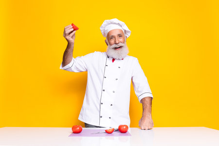 Cheerful mature chef showcasing fresh ingredients in a vibrant culinary settingの写真素材